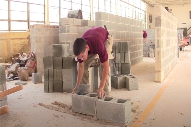 Worker in masonry shop building cinder block wall.