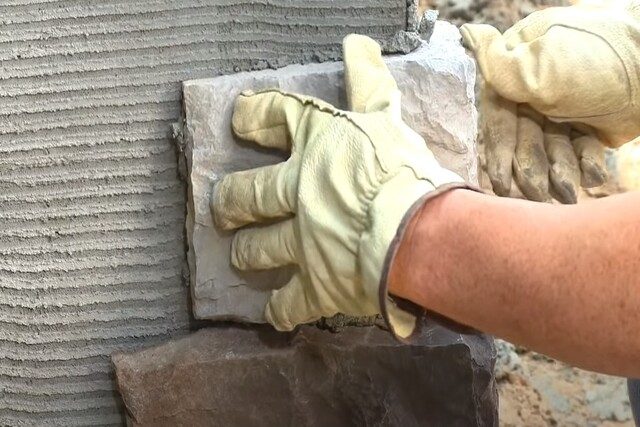 Veneer stone installation by worker with gloves on